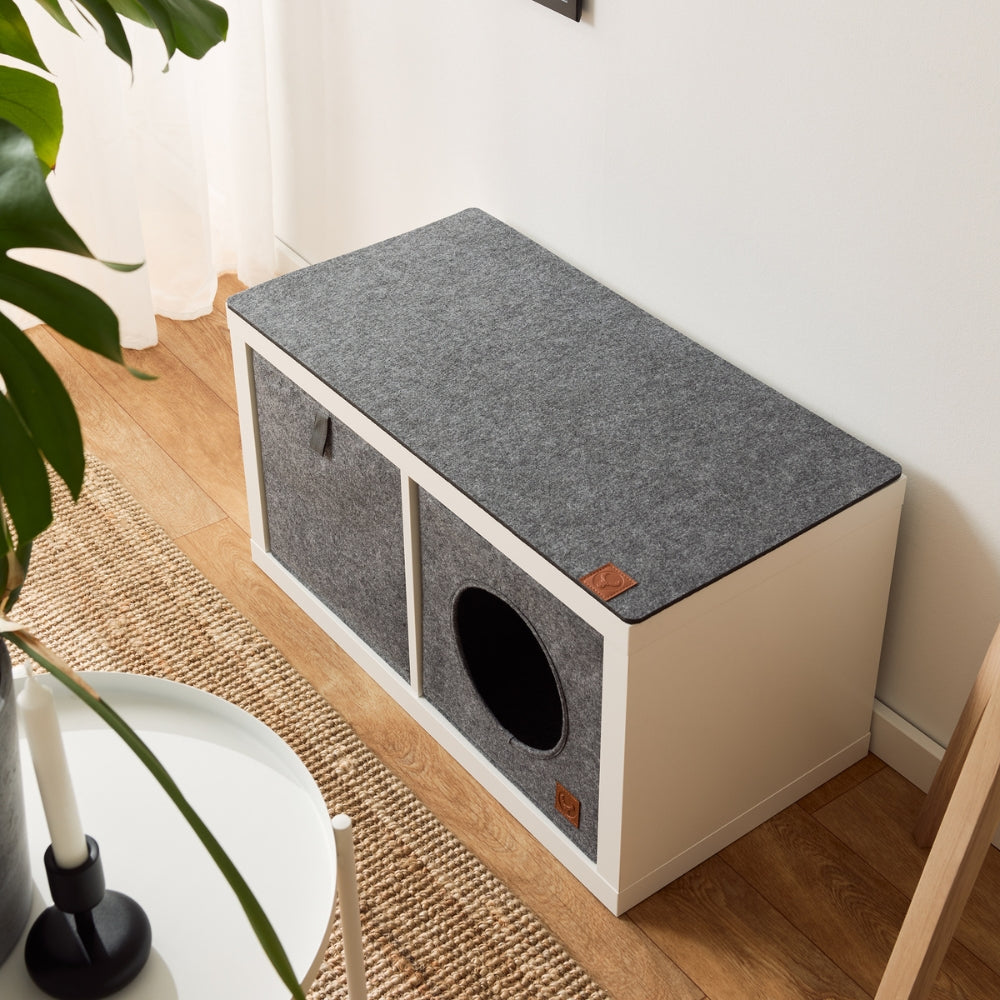 Weißes 2er Kallax Regal von IKEA mit Aufbewahrungsbox, Katzenkorb und Sitzauflage aus Filz.