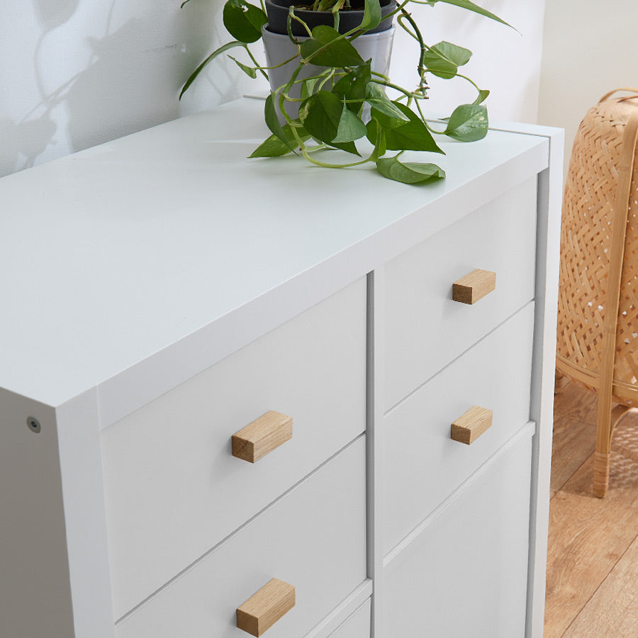 Ein weißes IKEA Kallax Regal mit Schubladeneinsätzen, an denen rechteckige Möbelgriffe aus Eiche montiert sind.
