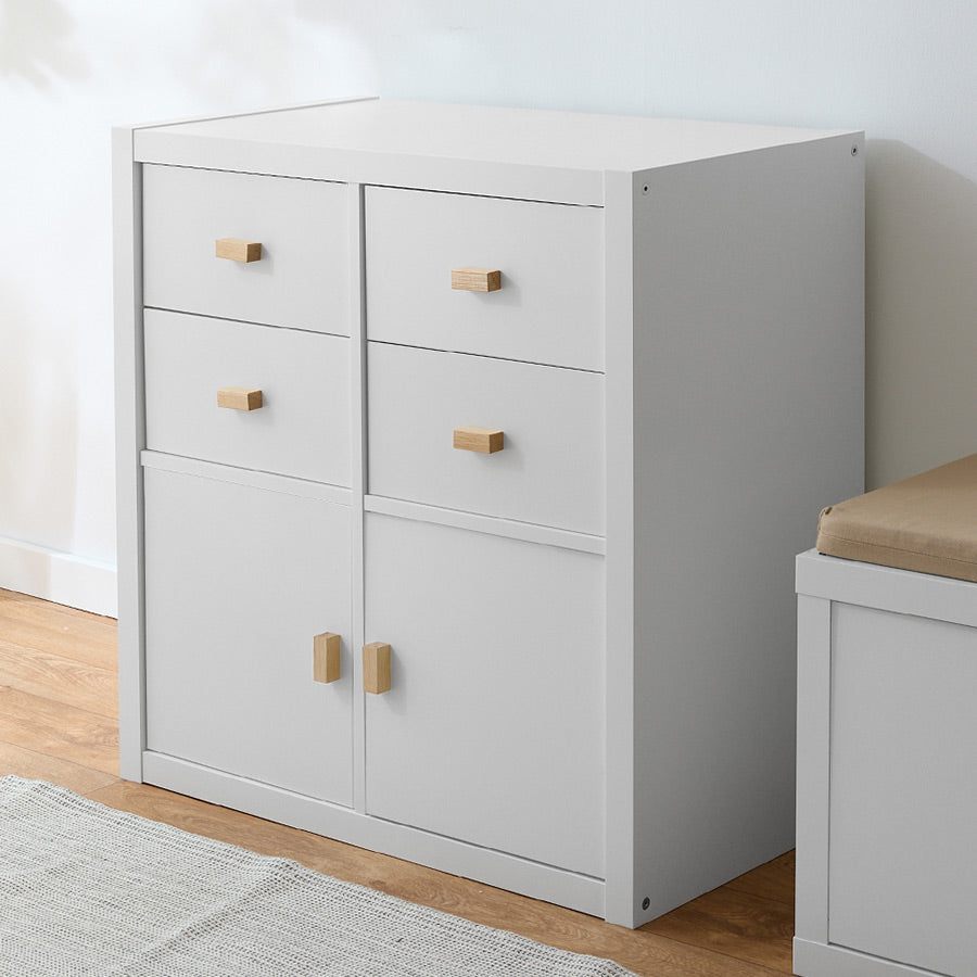 Ein weißes Kallax Regal von IKEA wurde mit Schubladen und Türen optimiert. An Schubladen und Türen sind eckige Holzgriffe aus Eiche befestigt.