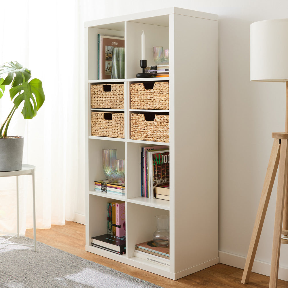 Weißes IKEA Kallax mit 4 Körben aus Wasserhyazinthe mit verschiedenen Griffen in einem Wohnzimmer.