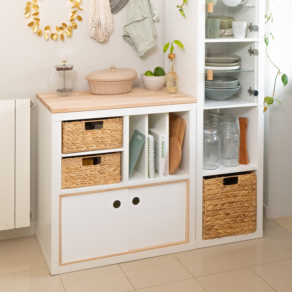 2 weiße IKEA Kallax Regale mit Zubehör, wie Flechtkörbe, Facheinsatz und Schiebetür.