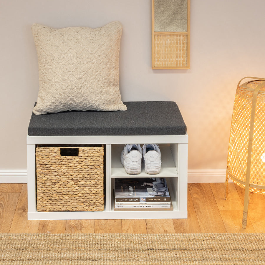 Kallax Sitzauflage auf einem 2er Kallax-Regal. Unten befinden sich Schuhe, Bücher und 1 Korb, oben ein beige farbenes Kissen.