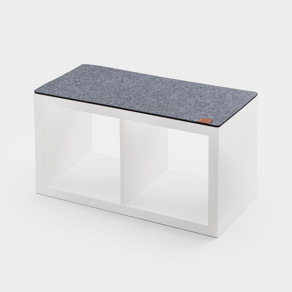 Eine graue Kallax Sitzauflage aus Filz auf einem weißen 2er Kallax Regal von IKEA.