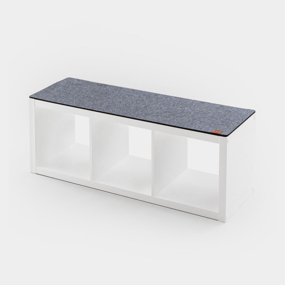 Graue Kallax Sitzauflage aus Filz, die auf einem weißen IKEA Kallax Regal mit 3 Fächern liegt.