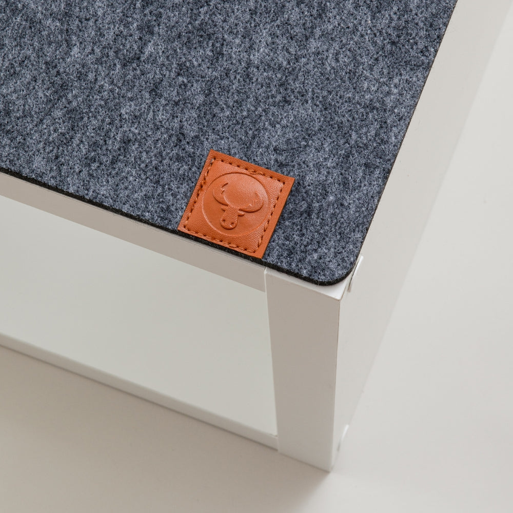 Detailaufnahme eines braunen New Swedish Design Logos aus braunem Leder auf einer Kallax Bankauflage aus grauem Filz.