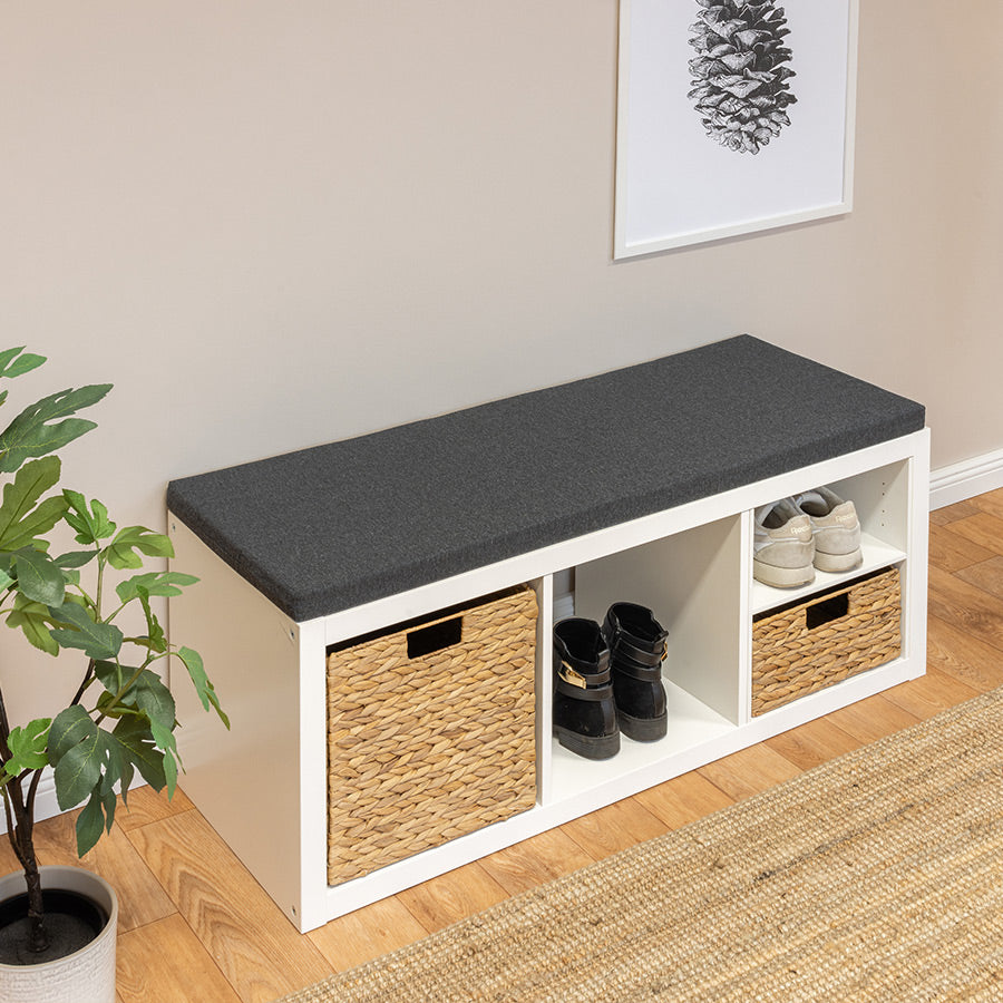 Ein 3er Ikea Kallax Regal liegt mit der langen Seite auf dem Boden, sodass es eine Sitzbank darstellt. Auf der Sitzbank liegt eine Sitzauflage in anthrazit. Die Regalfächer sind mit Körben und Schuhen gefüllt.